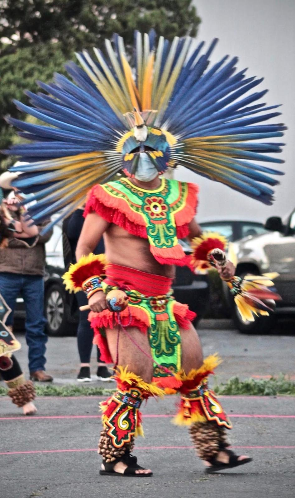 Aztec dancer in green and red regalia with blue feathered headdress
